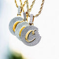 Three Cookies Pendants in yellow gold on matching 2mm Rope Chains hanging in front of blurred landscape. Circle pendants appear as though a bite has been taken out of the left side flooded in hand-set CZ stones with gold script c amongst the stones.