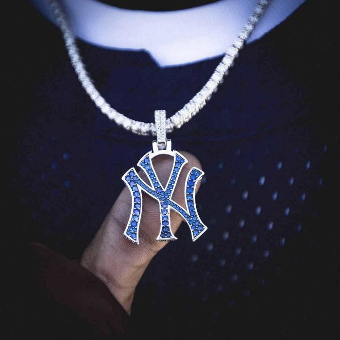 New York Yankees MLB logo pendant in 14k white gold plating with natural blue gemstones. Pictured on a 3mm Round Cut Tennis Necklace in White Gold, model holding pendant out on thumb to show detail.